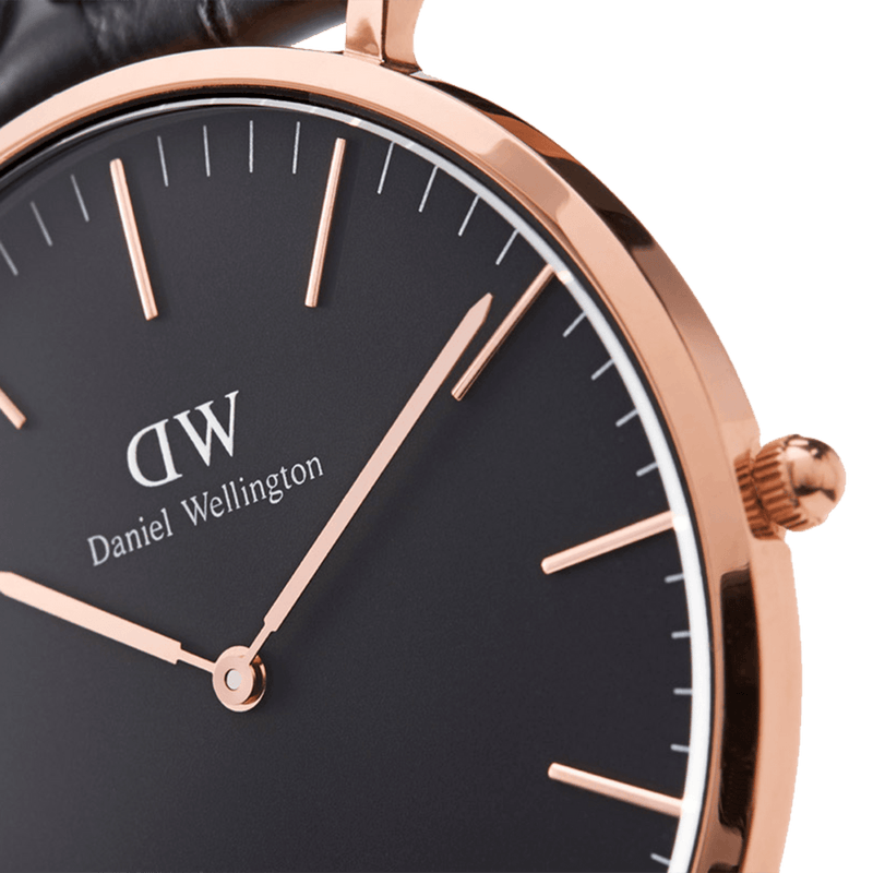 Elegant wristwatch with a black face and rose gold accents, displaying the brand ’Daniel Wellington’.