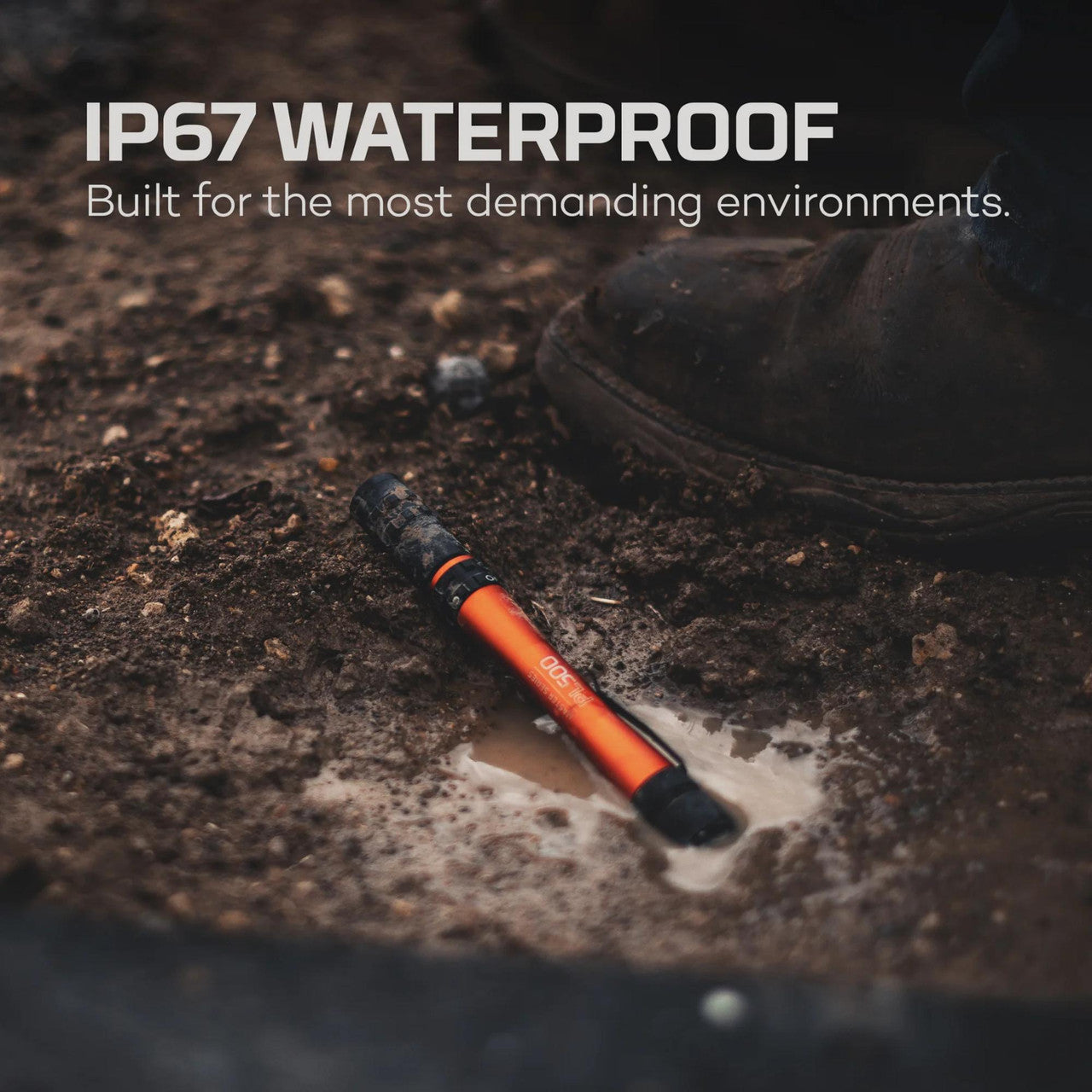 Orange and black waterproof flashlight or torch lying in muddy water.