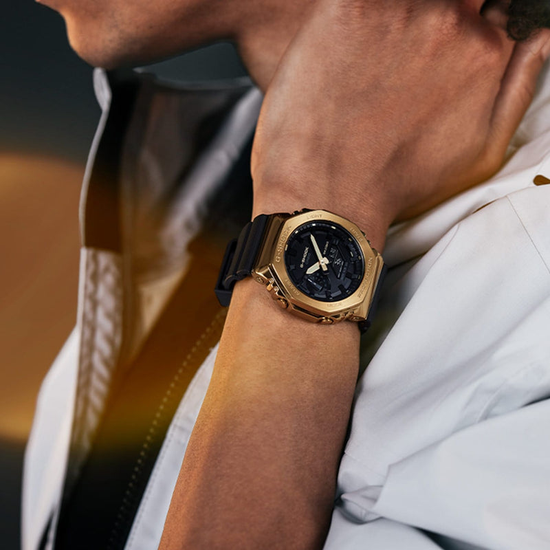 Gold-toned wristwatch with a black face and strap worn on a person’s wrist.