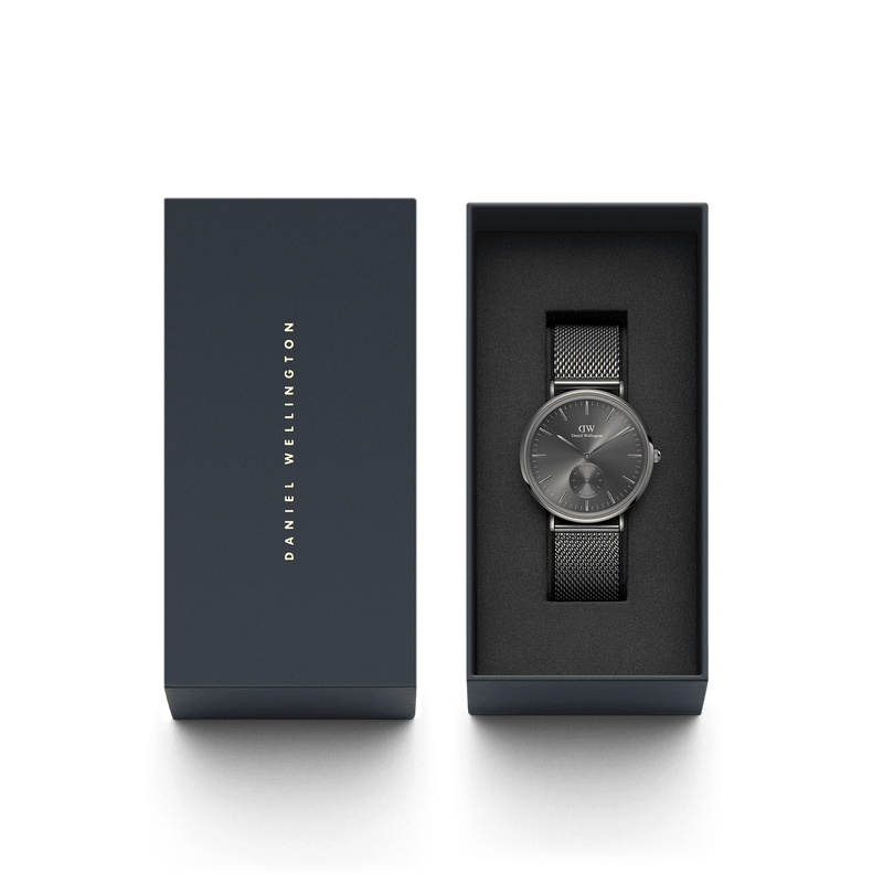 Sleek wristwatch with a dark face and mesh metal band in an open gift box.