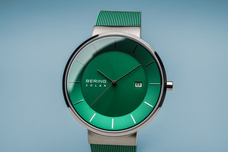 Green wristwatch with a circular face and mesh band.