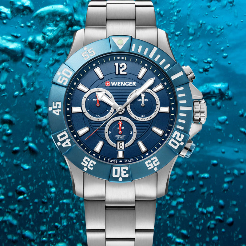 Stainless steel wristwatch with a blue dial and bezel against a watery backdrop.