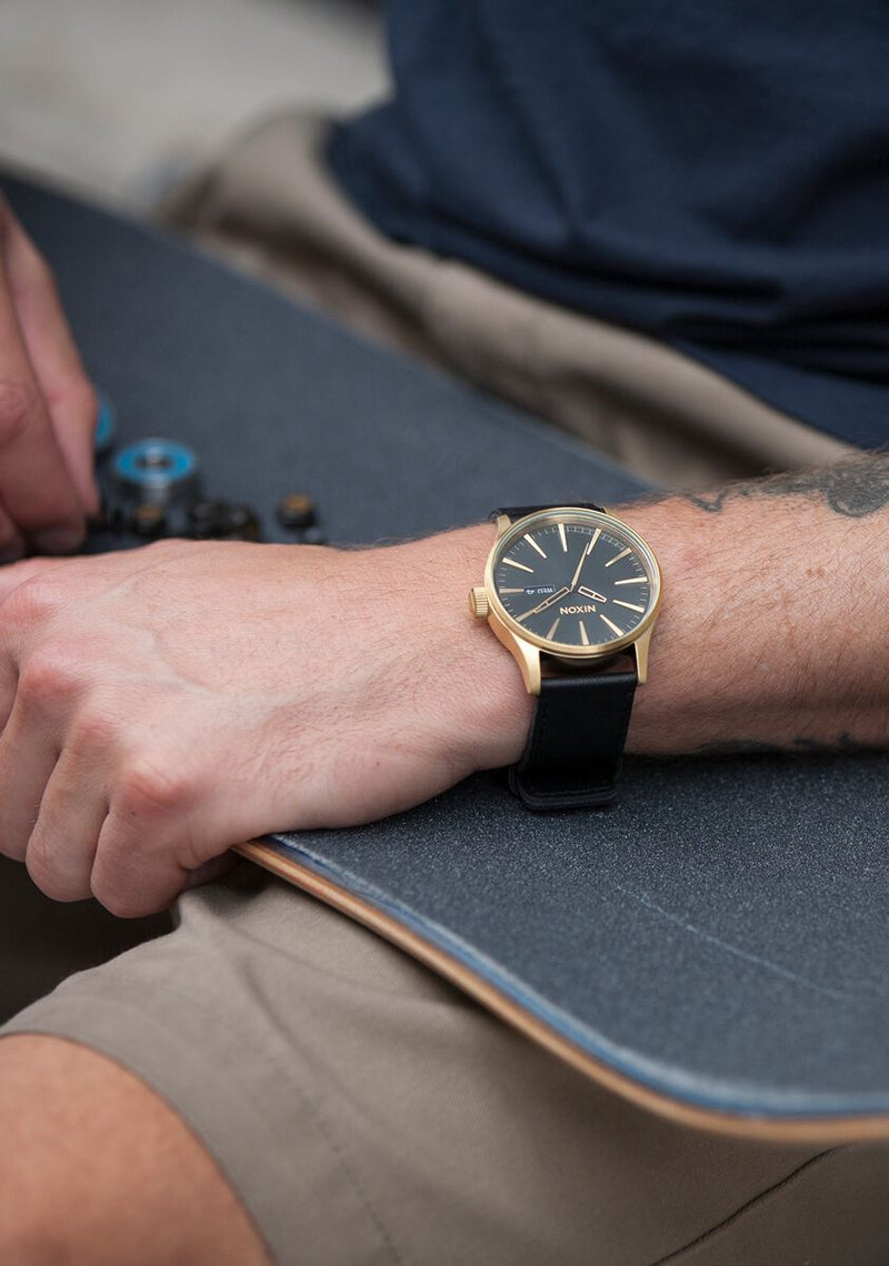 Wristwatch with a dark face and gold-toned case on a leather strap.