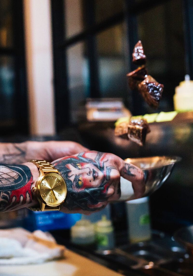 Tattooed arm wearing a gold watch.