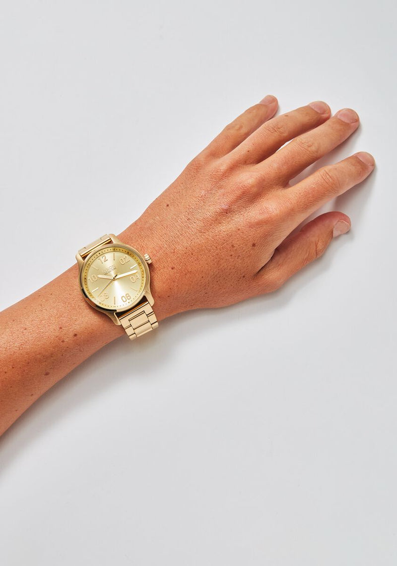Gold-toned wristwatch on a person’s wrist and hand.