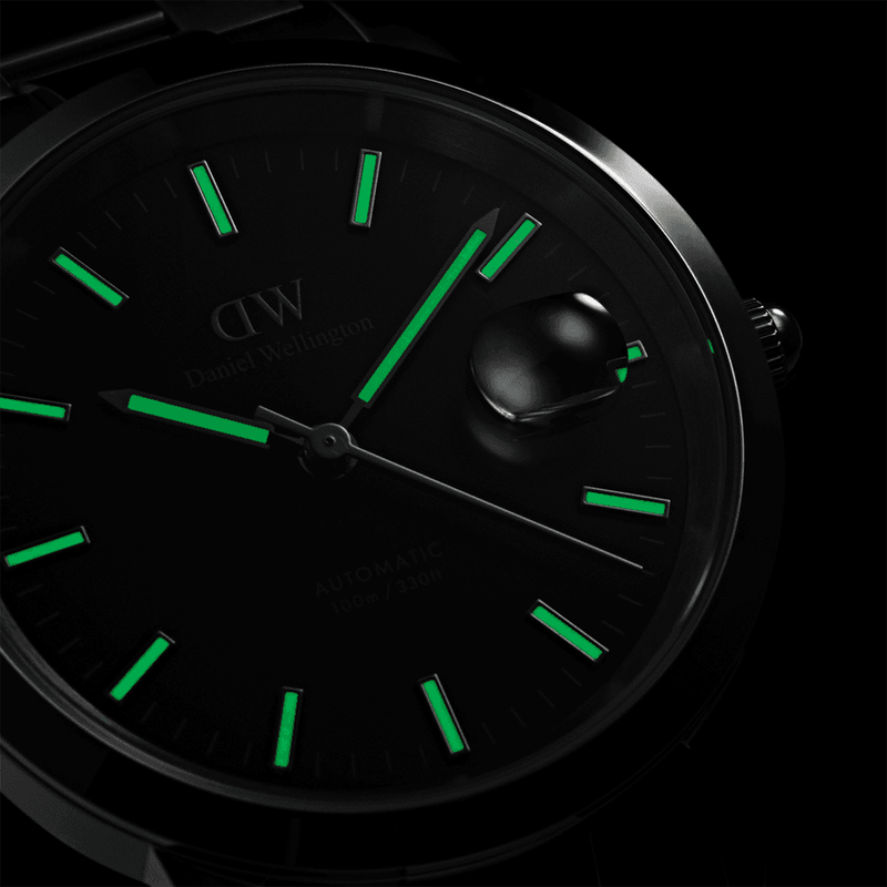 Analog watch face with glowing green hour markers and hands against a black background.