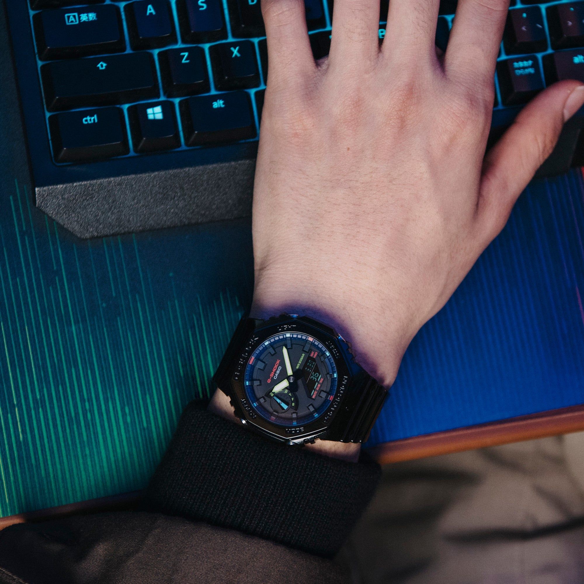 Wristwatch with a dark face and digital display worn on a hand resting on a keyboard.