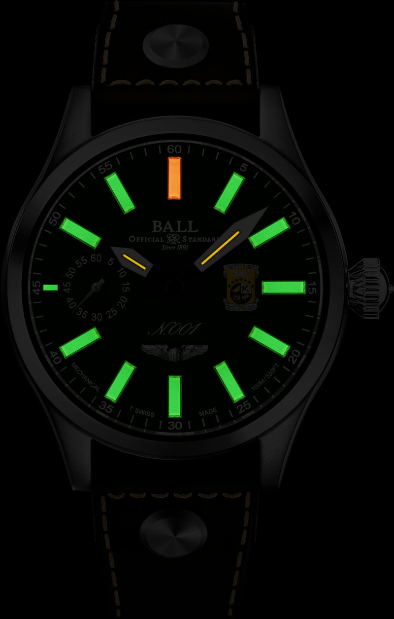 Wristwatch with glowing green hour markers and one orange marker in a dark setting.