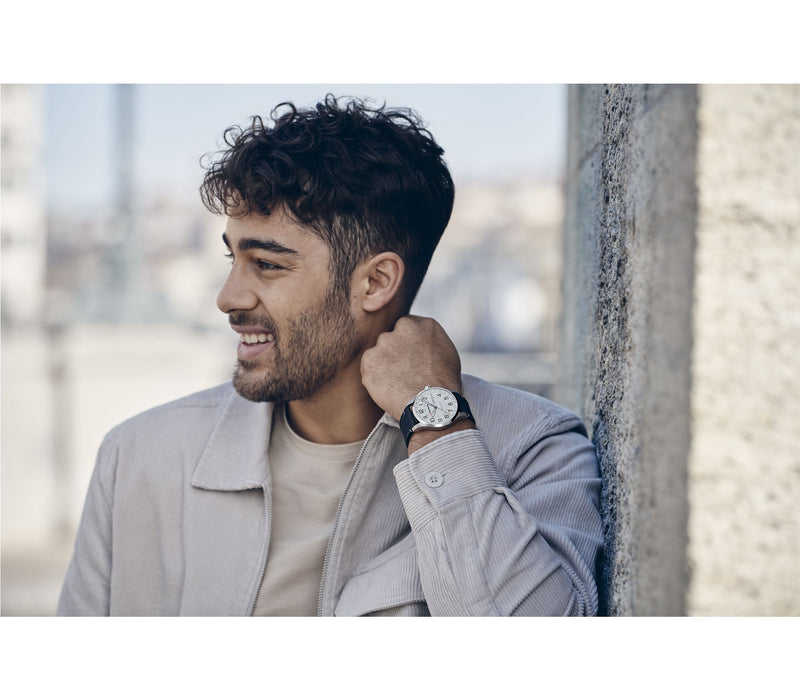 Smiling man with short dark hair wearing a light-colored jacket and wristwatch.