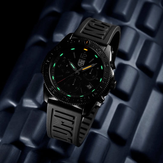 Black wristwatch with luminous green and orange markers on the dial and a textured rubber strap.